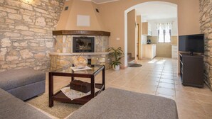 A living room with a stone wall, a fireplace, a sofa, a coffee table, and a television. - Beach front home in Tar-Vabriga (Tar-Vabriga)