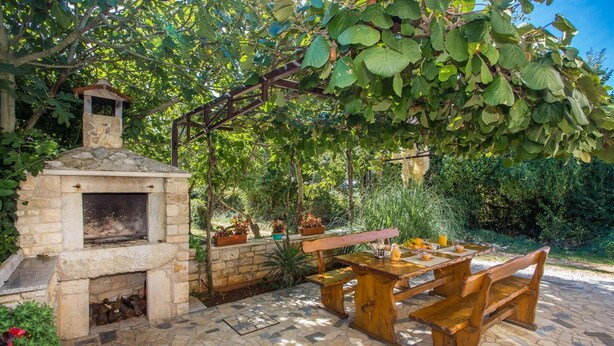 An outdoor patio with a stone fireplace, wooden benches, and a pergola covered with foliage. - Beach front home in Tar-Vabriga (Tar-Vabriga)