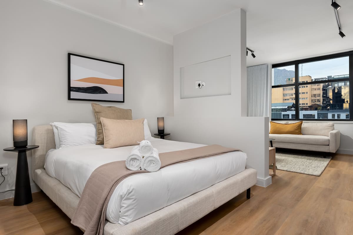 Een moderne hotelkamer met een groot bed, een bank, uitzicht op de stad en een schilderij aan de muur.