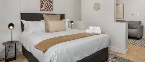 A modern bedroom with a large bed, a bedside lamp, a decorative wall piece, and a clock.