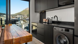 A modern kitchen with a built-in washer, a wooden bench, and a view of a cityscape through large windows.