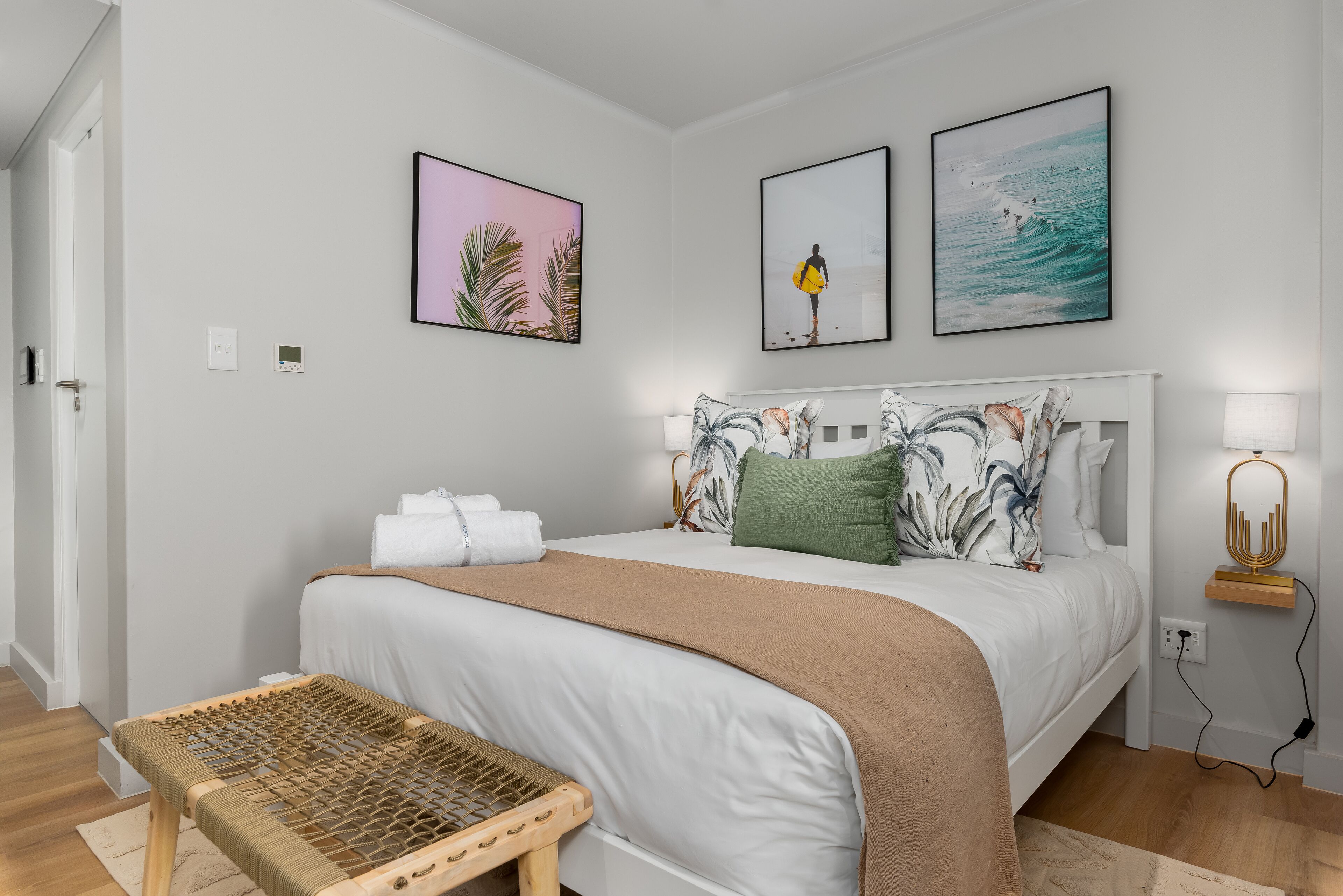 A bedroom with a bed, pillows, a bedside table, and artwork on the wall.