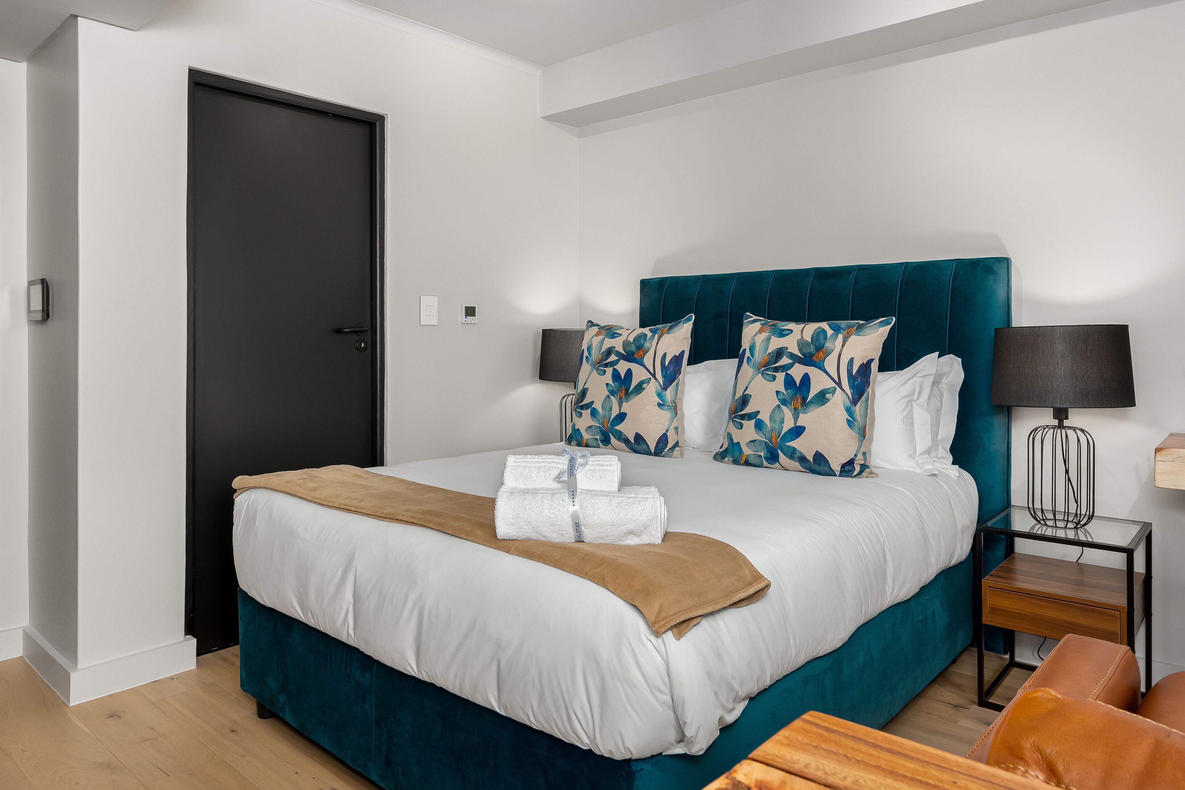 Una cama bien tendida con un cabecero color turquesa, ropa de cama blanca y almohadas estampadas con motivos florales.