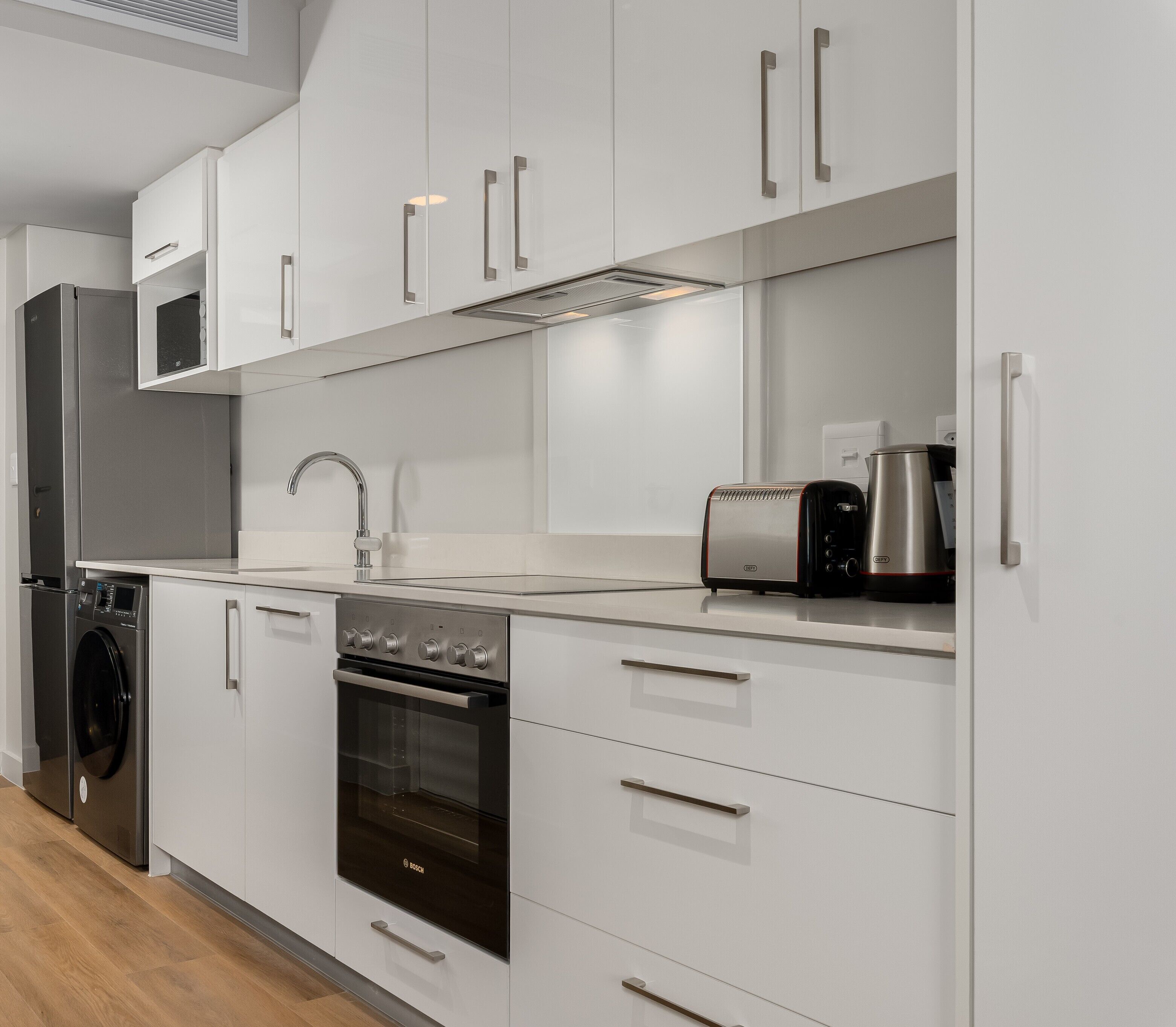 A modern kitchen with stainless steel appliances, white cabinetry, and a built-in oven.