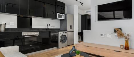 A modern kitchen with black cabinets, a microwave, and a washing machine. There is a wooden dining table with a plant and a candle.