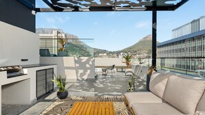 A modern rooftop terrace with a sofa, dining area, and potted plants.