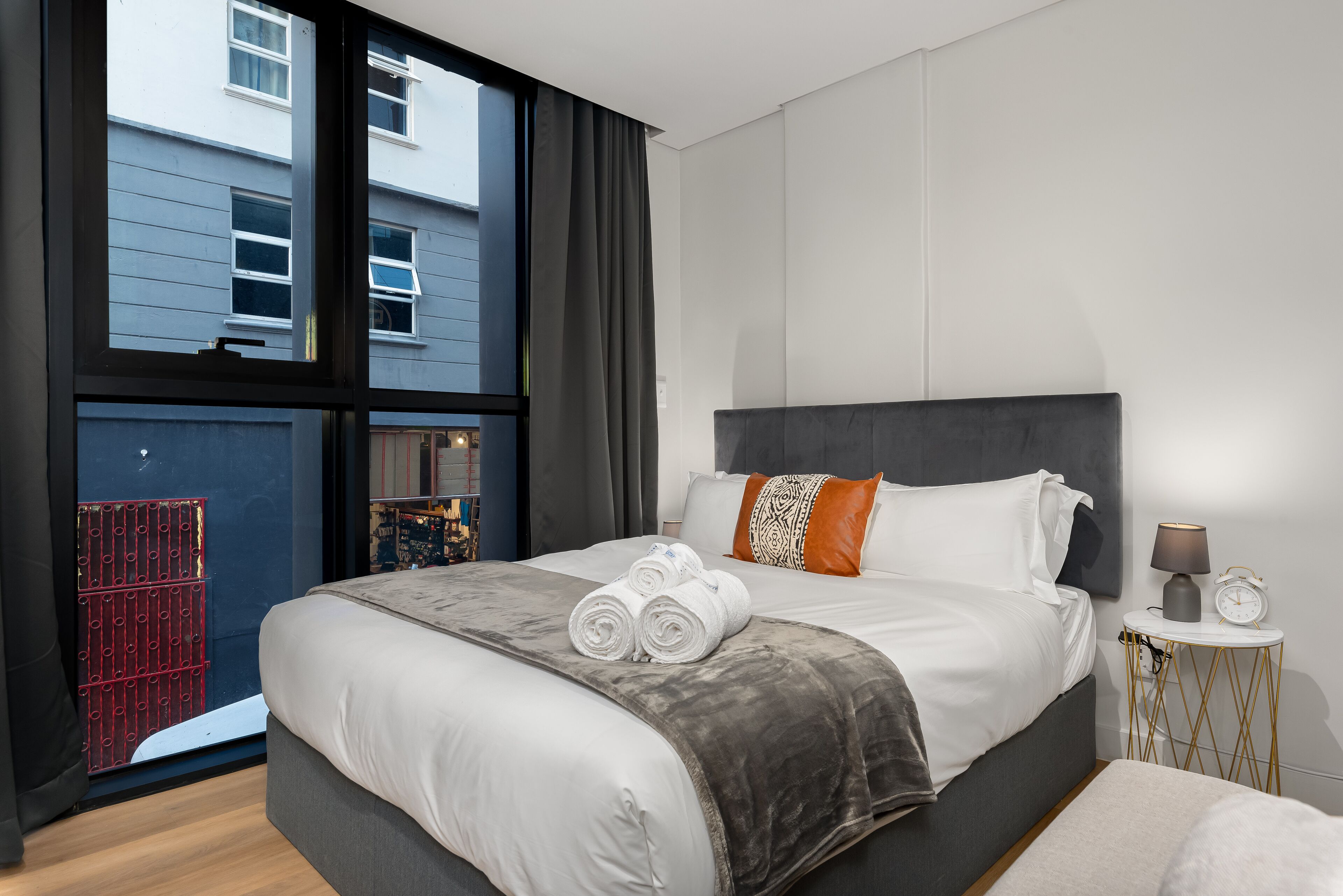 A modern hotel room with a large bed, a bedside table, and a view of the outside.