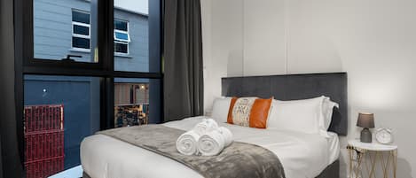 A modern hotel room with a large bed, a bedside table, and a view of the outside.