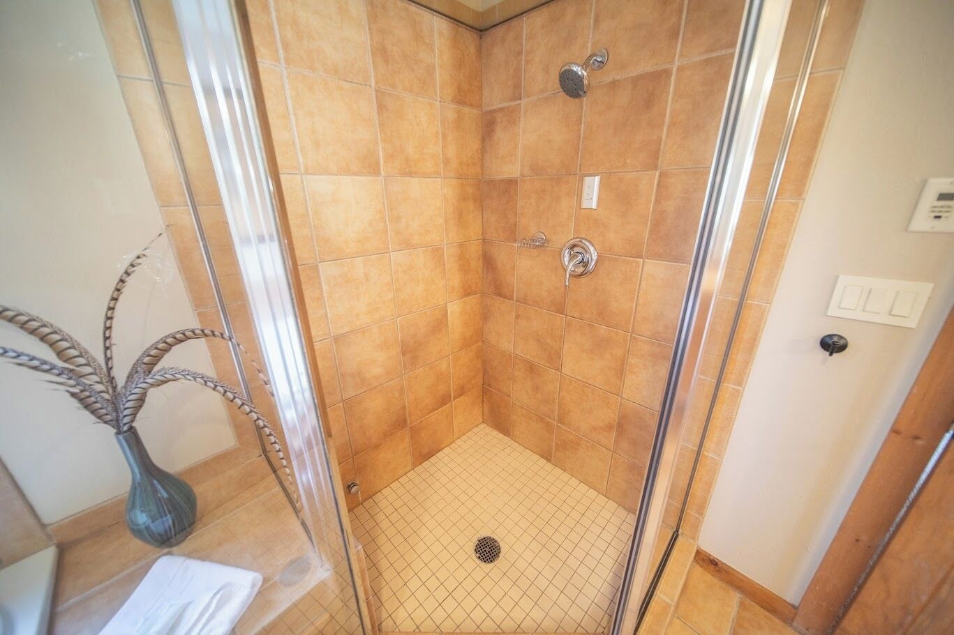 Eine begehbare Dusche mit Glaswänden, beigefarbenen Fliesen, einem Metall-Duschkopf und einem Ablauf.