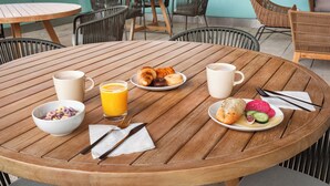 A round wooden table with breakfast items including croissants, a bowl of fruit, a glass of orange juice, and a plate with a croissant, a pastry, and some berries. - B&B Hotel Olhao Algarve (Olhao)