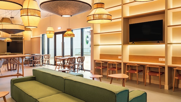 A modern interior with a green sofa, wooden tables, wicker lamps, and a flat-screen TV. - B&B Hotel Olhao Algarve (Olhao)