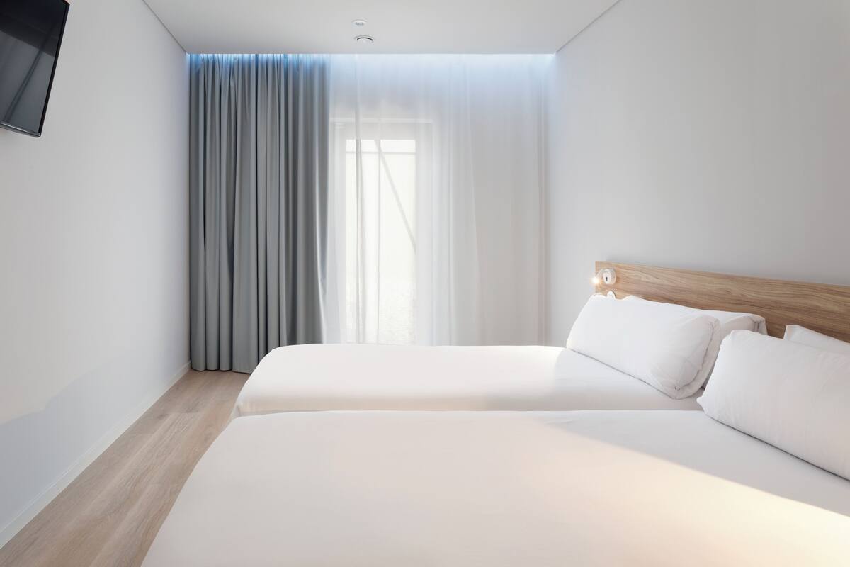 A modern hotel room with a large bed, a TV mounted on the wall, and a window with curtains.