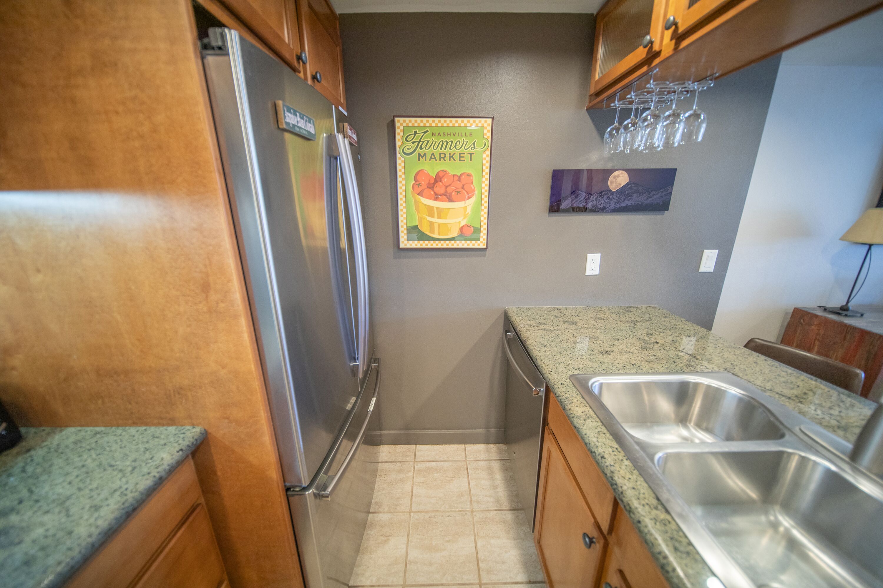 A kitchen with wooden cabinets, a stainless steel refrigerator, a granite countertop, and a double sink.