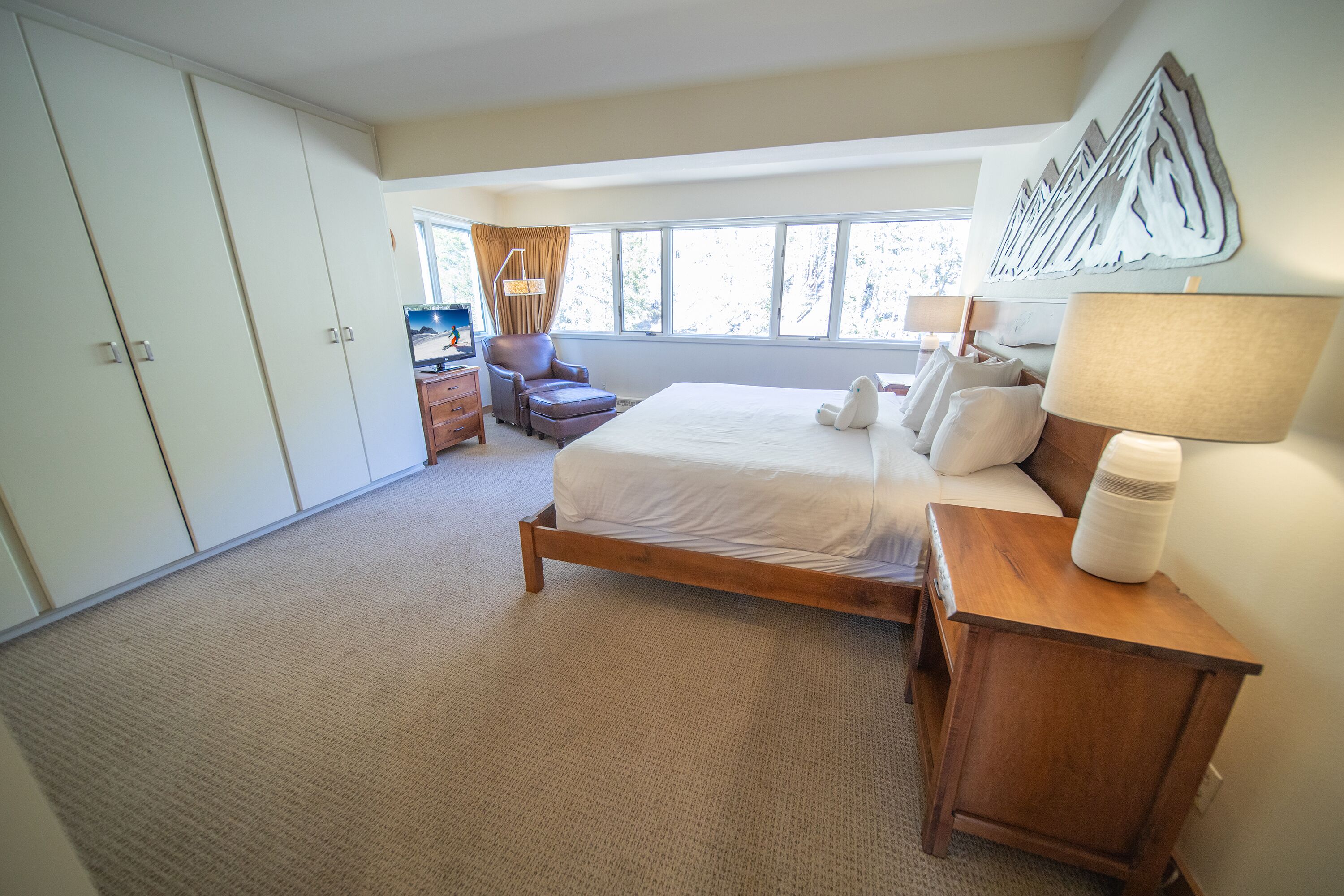 A bedroom with a large bed, a wooden nightstand, a chair, a dresser, and a window with curtains.