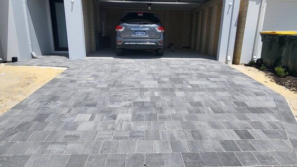 Een garage met een grijze SUV erin, een geplaveide oprit die naar de garage leidt, en een helderblauwe lucht met wolken.