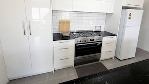 Een moderne keuken met witte kasten, een gasfornuis, een oven en een koelkast.