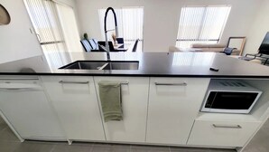 Een moderne keuken met witte kasten, een zwart aanrecht, een ingebouwde magnetron en een raam met blinds.