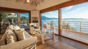 A spacious living area with a large window overlooking a body of water, a pool, and a deck. - Seafront Marine Villa: Seaside Elegance, 30m from the Shore (Sivota)