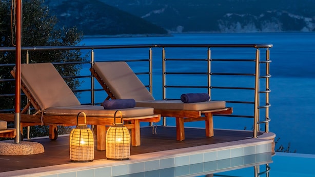 An infinity pool with lounge chairs and umbrellas, overlooking a mountainous landscape. - Seafront Marine Villa: Seaside Elegance, 30m from the Shore (Sivota)