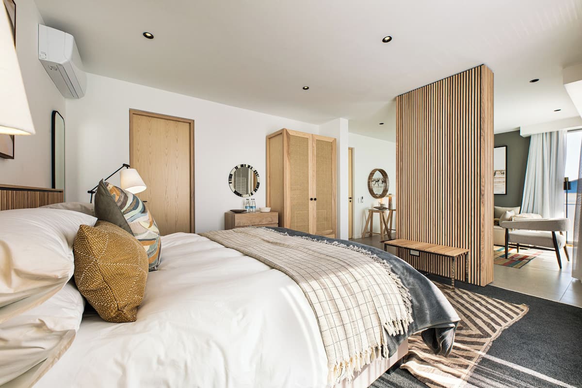 A modern hotel room with a large bed, a wooden wardrobe, a desk, and a seating area.