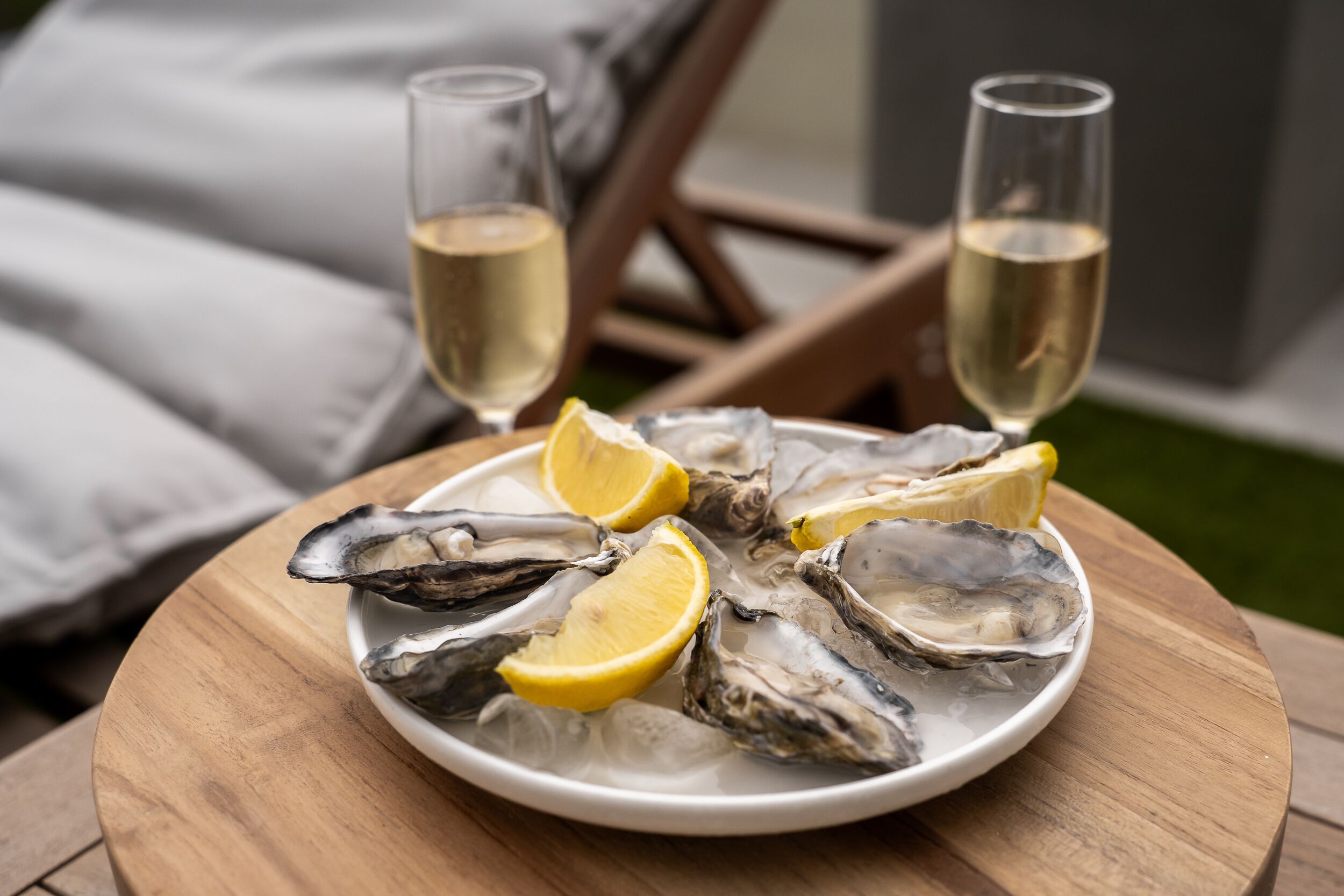 A plate of oysters with lemon wedges and two glasses of white wine on a wooden table.
