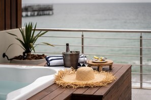 A wooden deck with a hot tub, a straw hat, a metal bucket, and a small table with a plate and glasses. - The Pearls Beach Pods (Swakopmund)