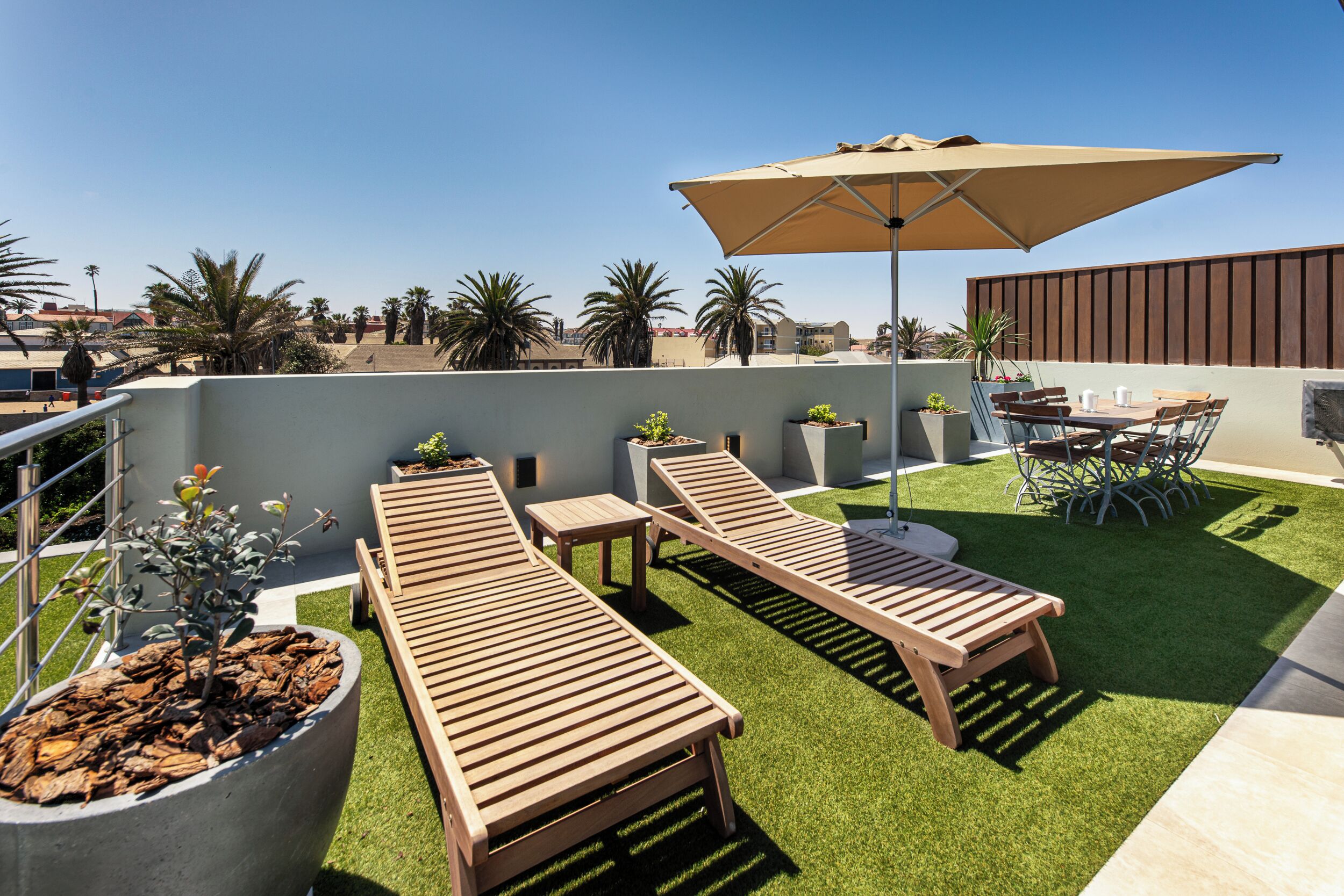 A rooftop terrace with wooden loungers, a table, and chairs under a large umbrella.