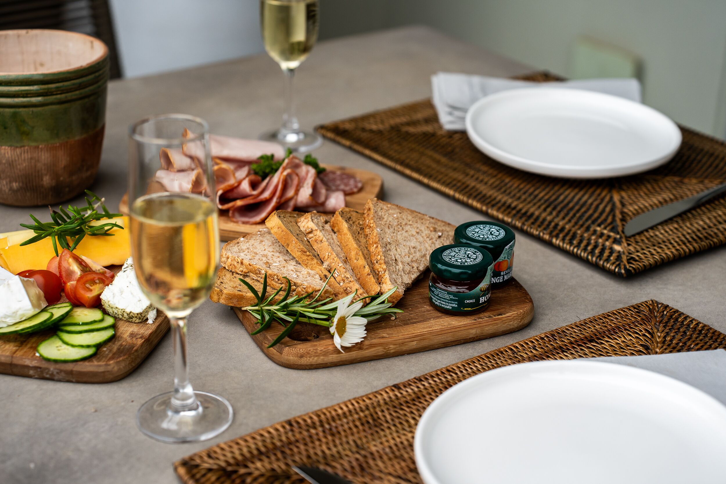Una mesa con diversos alimentos, incluyendo queso, pan y embutidos, acompañada de una copa de vino blanco.