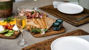 Una mesa con diversos alimentos, incluyendo queso, pan y embutidos, acompañada de una copa de vino blanco.