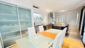 Une cuisine moderne avec un coin repas, comprenant une table en verre, des chaises blanches et un plancher en bois.