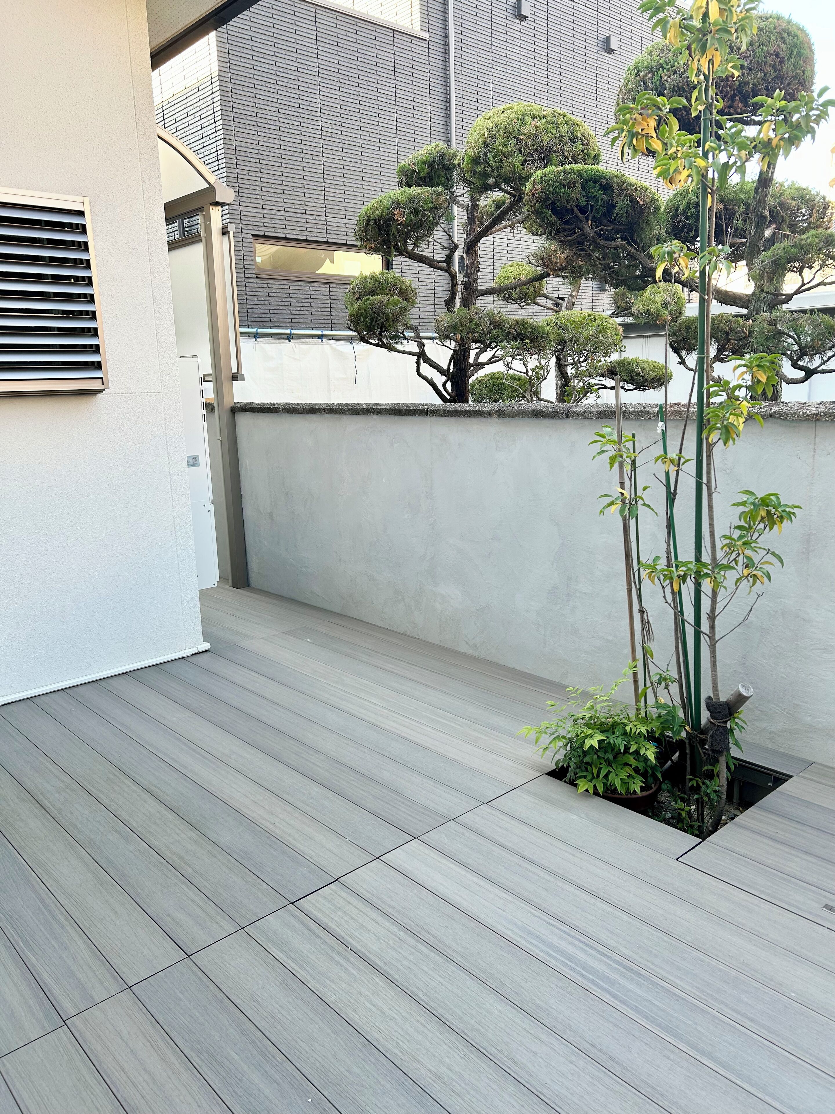 Un balcon avec un plancher en bois, une plante en pot et, au fond, un immeuble à la façade en briques.