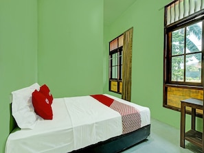 A single bed with white and red bedding, a wooden nightstand, a window with a view of greenery, and a green wall.