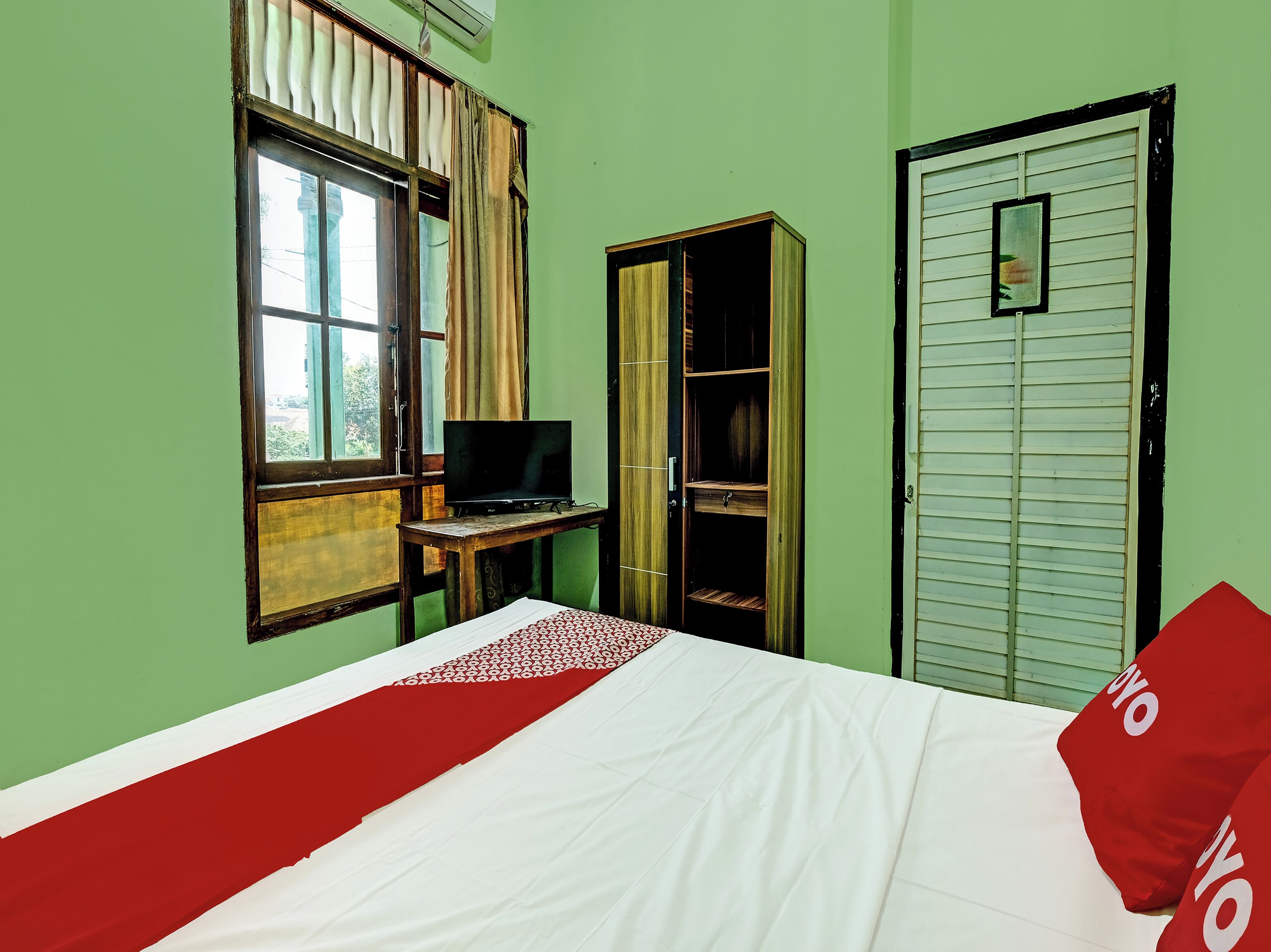 A room with a bed, a desk with a TV, a wardrobe, and a door with a mirror.