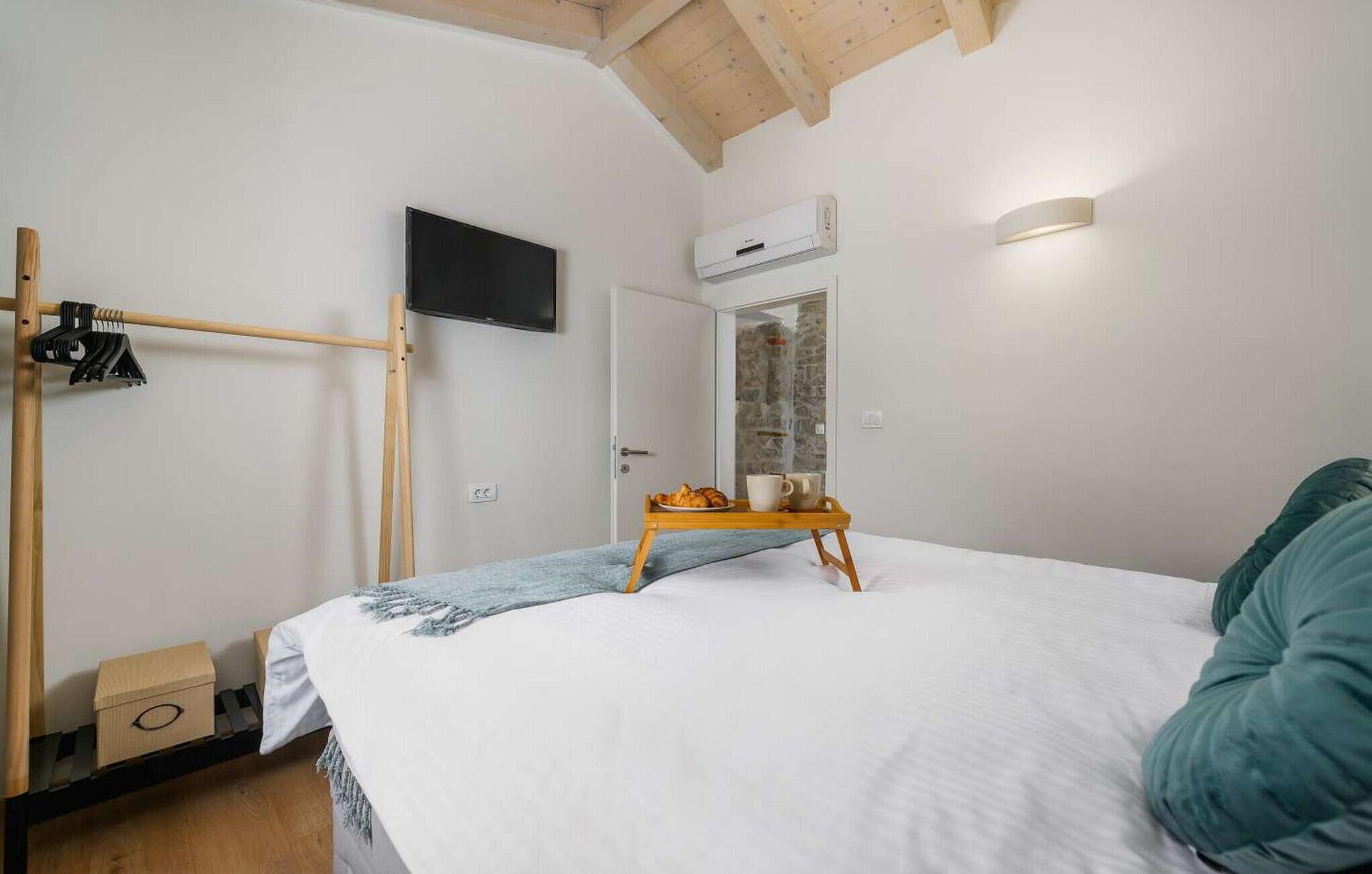 Een slaapkamer met een bed, een houten plank, een televisie, een airconditioner en een raam met uitzicht op een stenen muur.