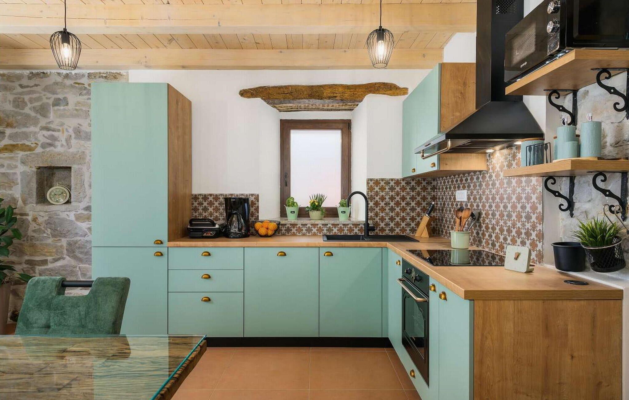 Een keuken met lichtgroene kastjes, een stenen muur, een houten plafond en een inbouwoven.