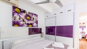 Une chambre d’hôtel moderne équipée d’un lit, d’un grand miroir, d’une armoire et d’un ventilateur de plafond.