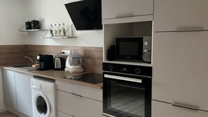 A modern kitchen with a washing machine, microwave, oven, and a flat-screen TV mounted on the wall. - Appartement-loft de Centre-ville (Montélimar)