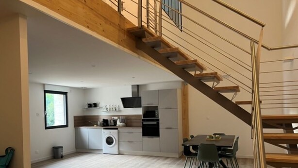 A spacious kitchen with a dining area, a staircase, and a washing machine. - Appartement-loft de Centre-ville (Montélimar)