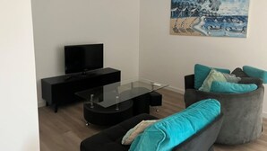A modern living room with a flat-screen TV, a glass coffee table, and a sofa with teal cushions. - Appartement-loft de Centre-ville (Montélimar)