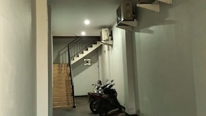Un couloir étroit avec un escalier menant à un palier. Deux motos sont garées contre le mur.