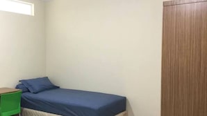 Une petite chambre avec un lit simple, une armoire en bois, une chaise verte et un bureau.