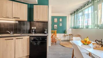A modern kitchen with light wood cabinets, a black dishwasher, and a teal accent wall.