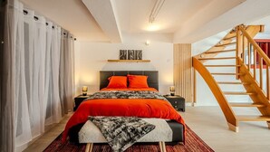 Een moderne slaapkamer met een groot bed, een houten trap en een nachtkastje met een lamp.