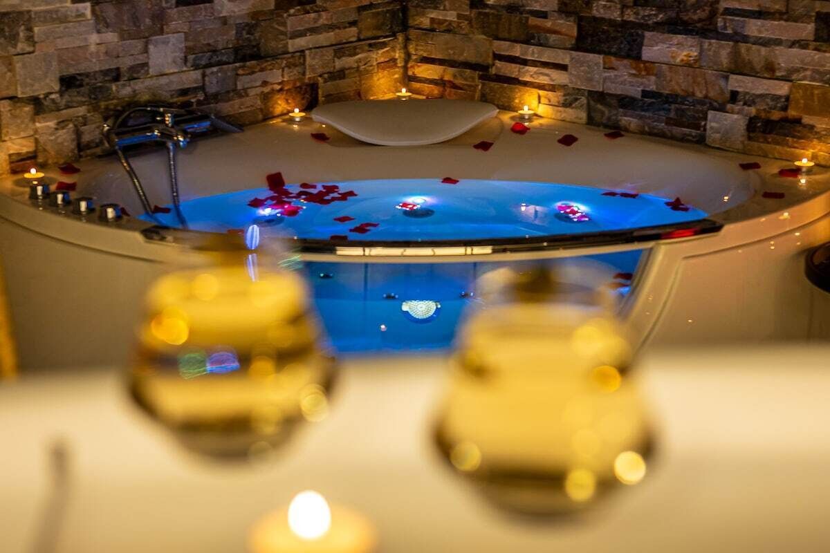 A spa area with a stone wall, a hot tub surrounded by rose petals, and candles.