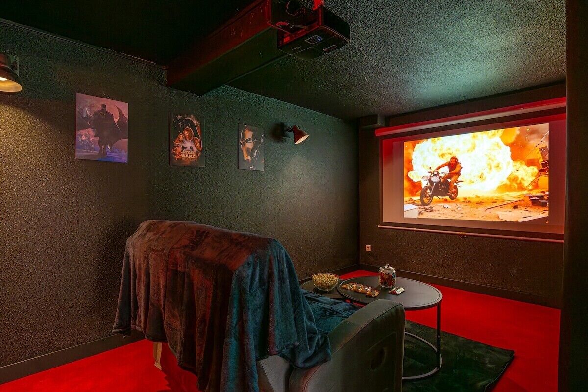 A room with a large screen displaying a movie scene, a small table with snacks, and a cozy seating area with a blanket.