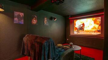 A room with a large screen displaying a movie scene, a small table with snacks, and a cozy seating area with a blanket.