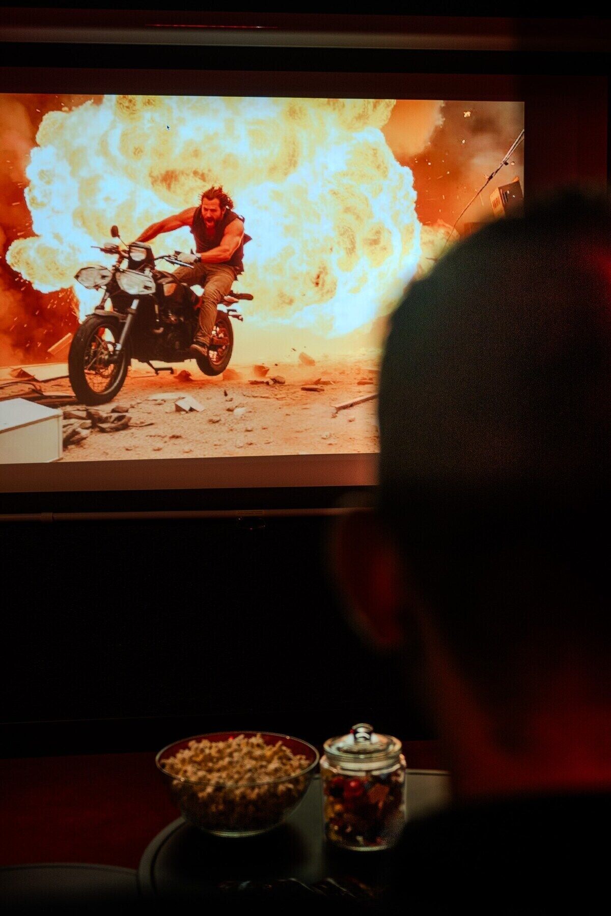 A person watching a movie on a large screen with popcorn and a drink on a tray in front of them.
