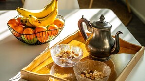 Een ontbijtplateau met fruit, noten en een theepot op een tafel in een kamer met stoelen en een groene wand.