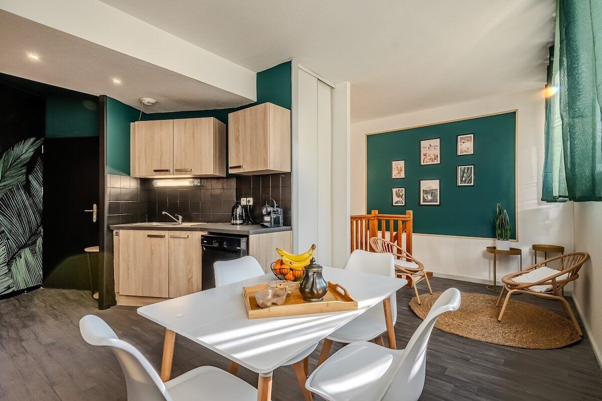 Une cuisine moderne avec des meubles en bois, un coin repas avec des chaises blanches et un mur d’accent de couleur turquoise orné de tableaux encadrés.