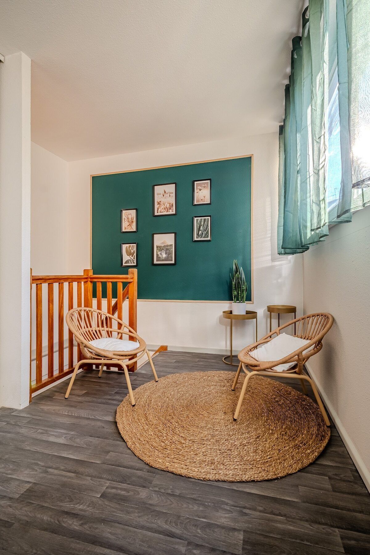 Una habitación con pared de acento color aguamarina, dos sillas de mimbre, un tapete redondo pequeño y una barandilla de madera.